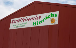 Rotes Gebäude mit einem Firmenschild, auf dem "Kartoffelvertrieb Hinrichs" steht.